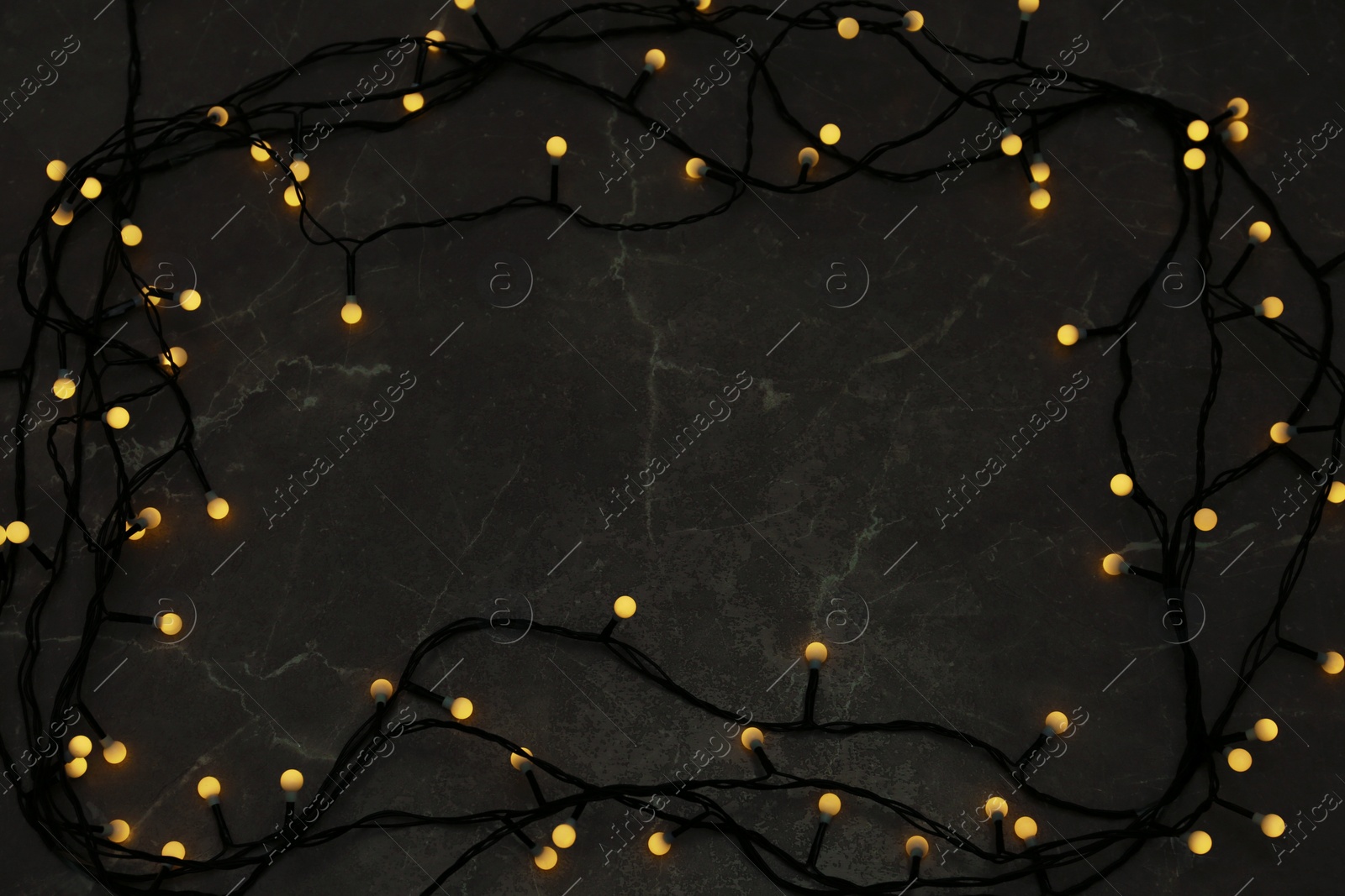 Photo of Frame made of glowing Christmas lights on grey marble background, top view. Space for text