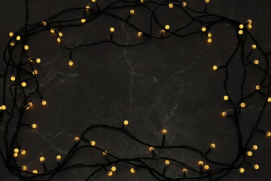 Frame made of glowing Christmas lights on grey marble background, top view. Space for text