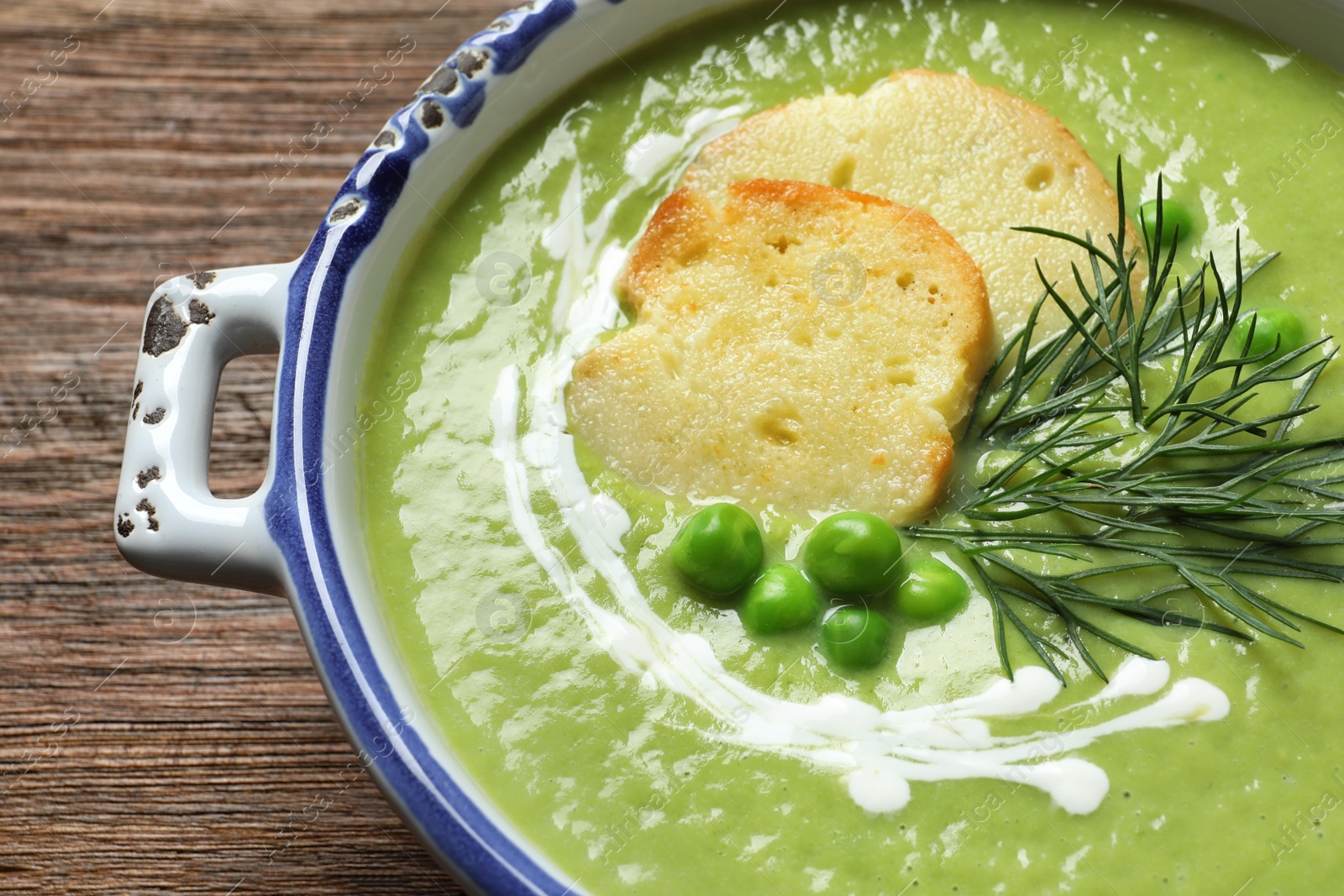 Photo of Fresh vegetable detox soup made of green peas with croutons in dish on wooden table, closeup