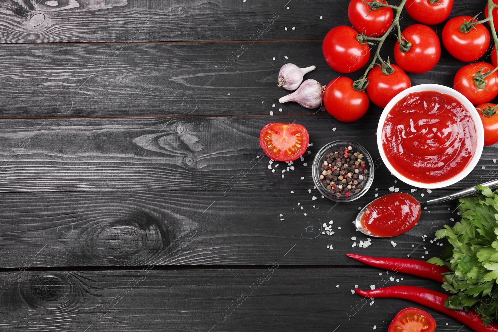 Photo of Flat lay composition with delicious ketchup, spices and products on black wooden table, space for text. Tomato sauce