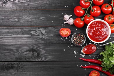Photo of Flat lay composition with delicious ketchup, spices and products on black wooden table, space for text. Tomato sauce