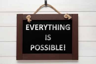 Image of Small chalkboard with motivational quote Everything is possible hanging on white wooden wall