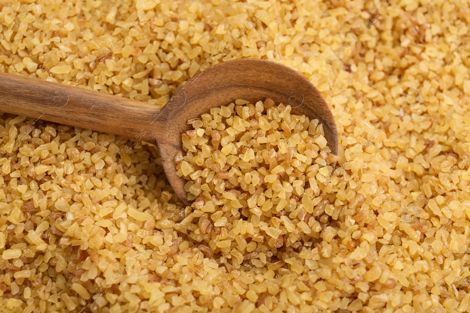 Photo of Wooden spoon on pile of uncooked bulgur, closeup