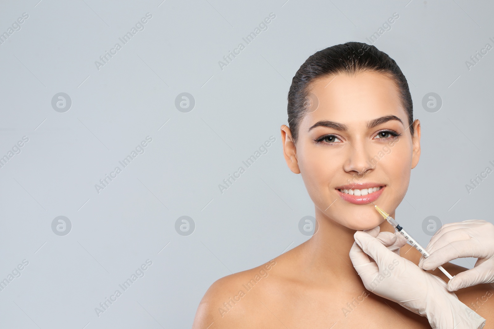 Photo of Young woman getting lips injection on grey background, space for text. Cosmetic surgery