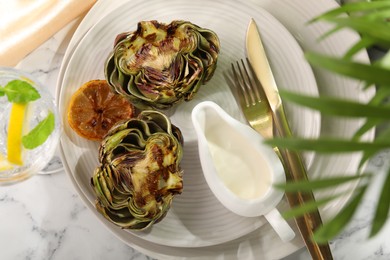 Photo of Tasty grilled artichokes served on white marble table, flat lay