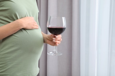 Photo of Future mother with glass of wine indoors, closeup. Alcohol abuse during pregnancy