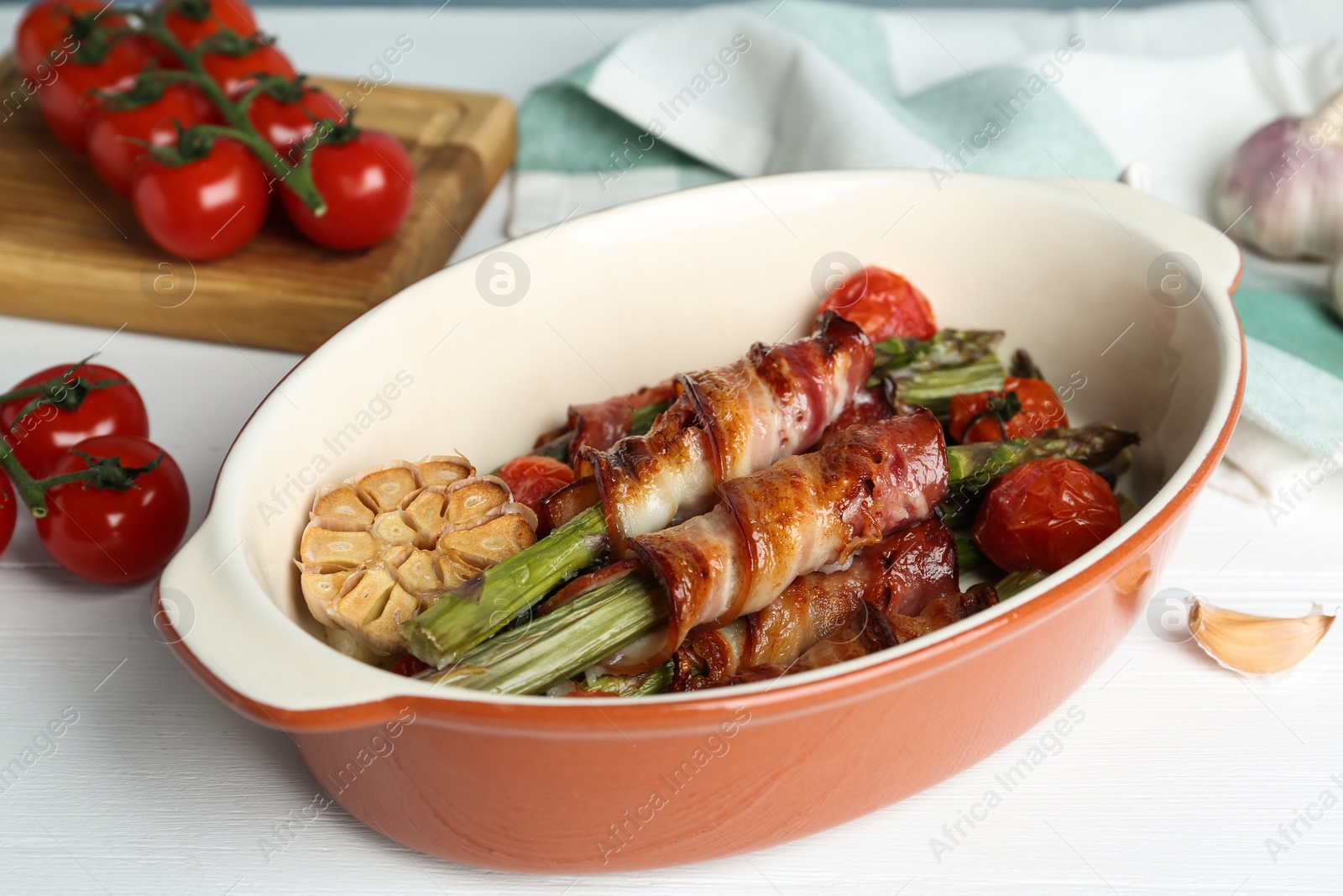 Photo of Oven baked asparagus wrapped with bacon in ceramic dish on white wooden table