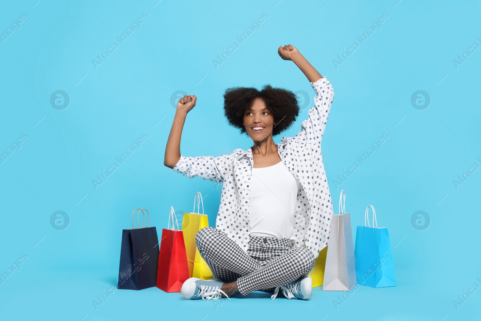 Photo of Happy African American woman with shopping bags on light blue background