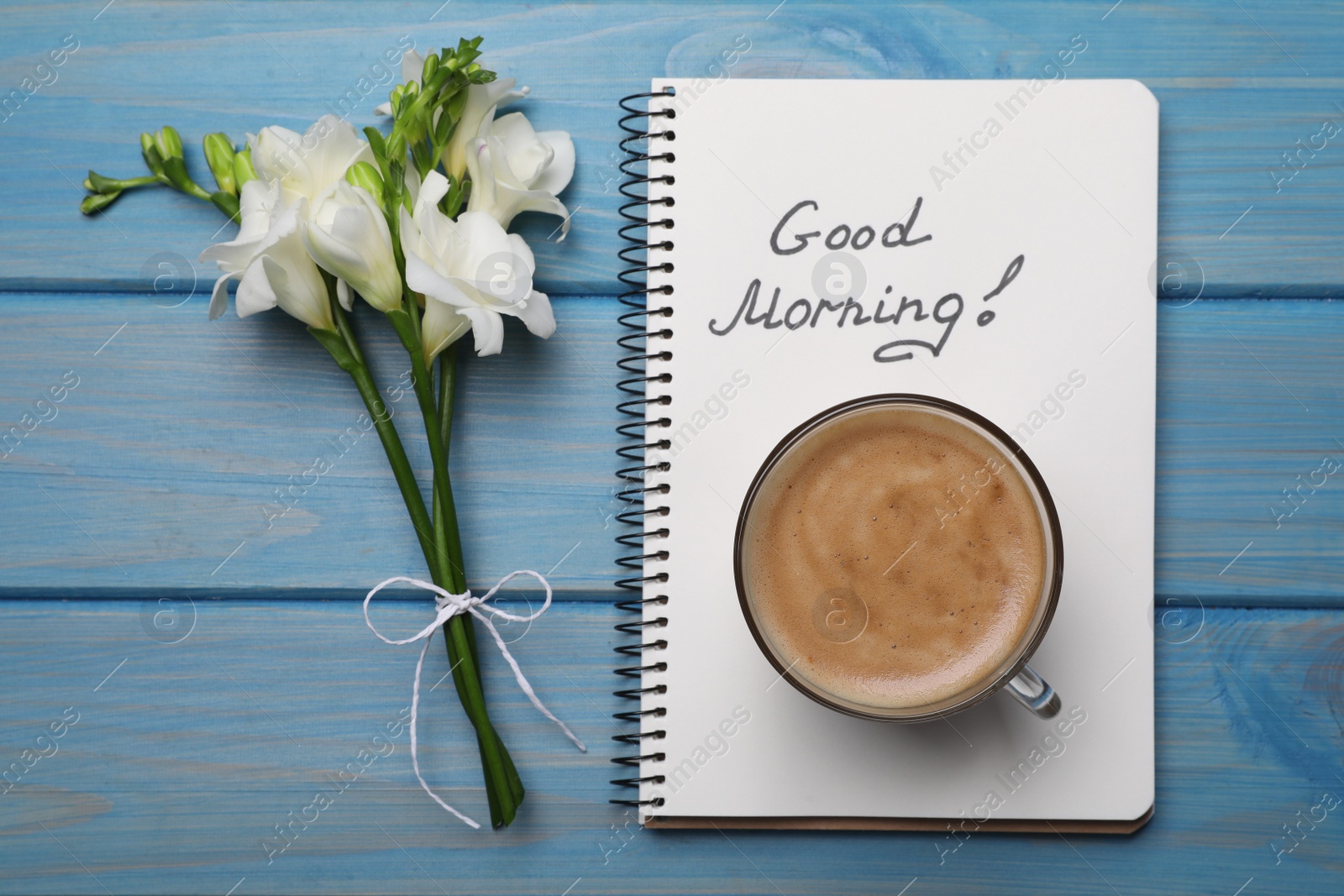 Photo of Aromatic coffee, flowers and Good Morning! message on light blue wooden table, flat lay