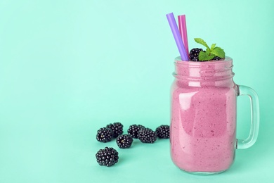 Photo of Mason jar of tasty blackberry smoothie with straws on turquoise background. Space for text