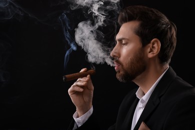 Photo of Handsome man smoking cigar on black background. Space for text