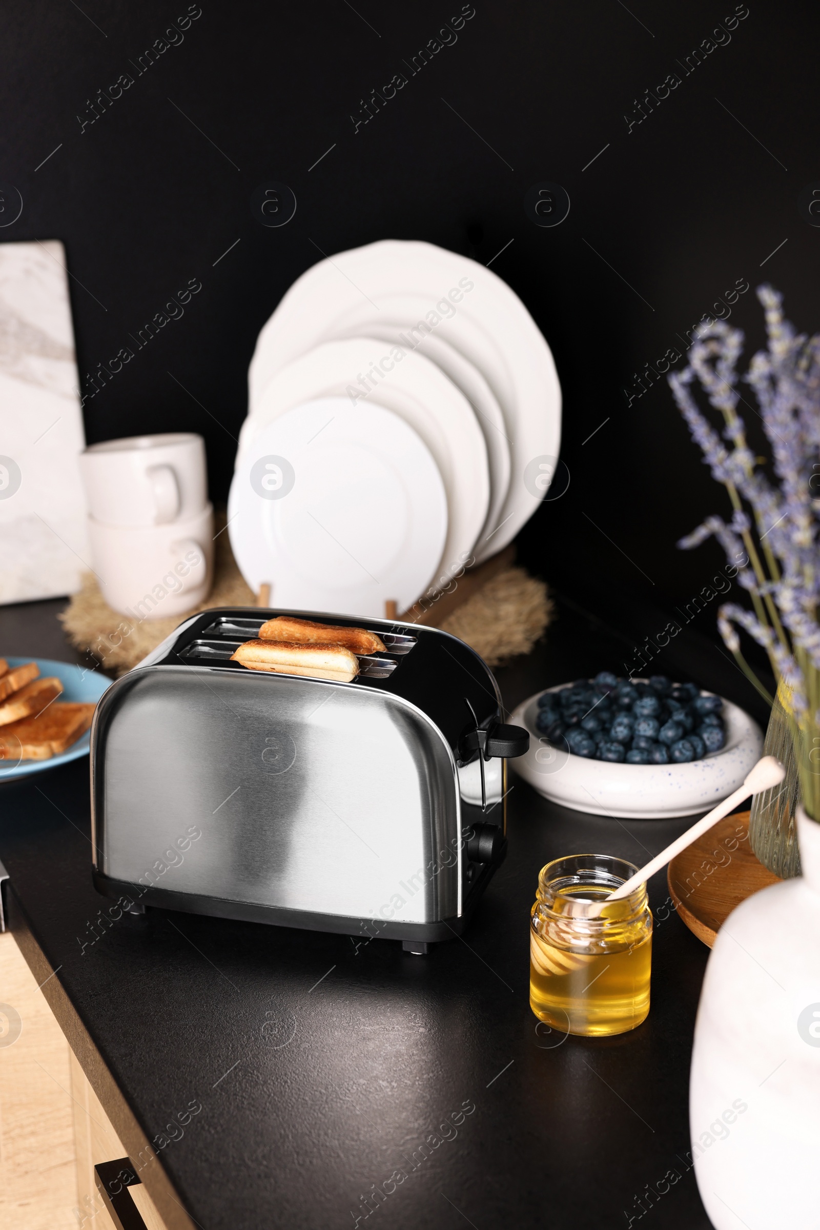 Photo of Toaster with roasted bread and honey on black countertop in kitchen