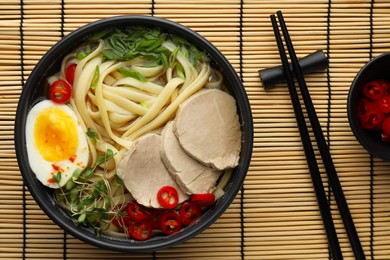 Delicious ramen with meat in bowl served on bamboo mat, flat lay. Noodle soup