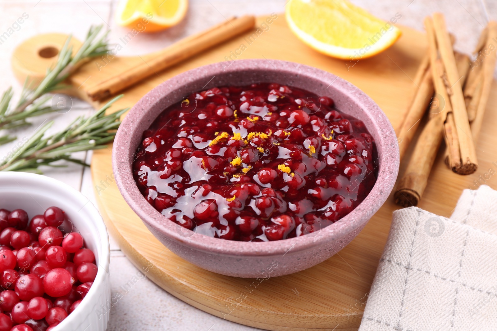 Photo of Tasty cranberry sauce in bowl and ingredients on white tiled table