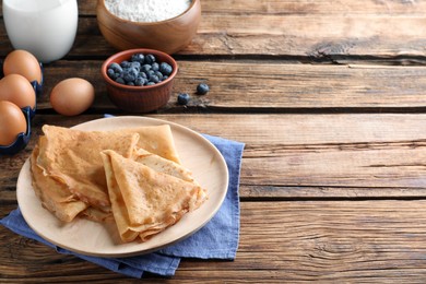 Photo of Delicious crepes and ingredients on wooden table. Space for text