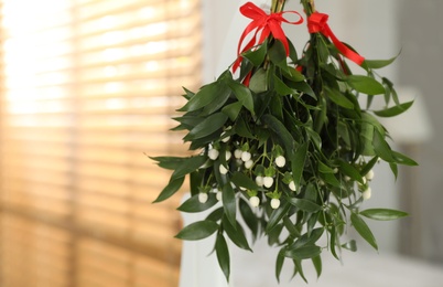 Photo of Mistletoe bunches with red bows hanging indoors, space for text. Traditional Christmas decor