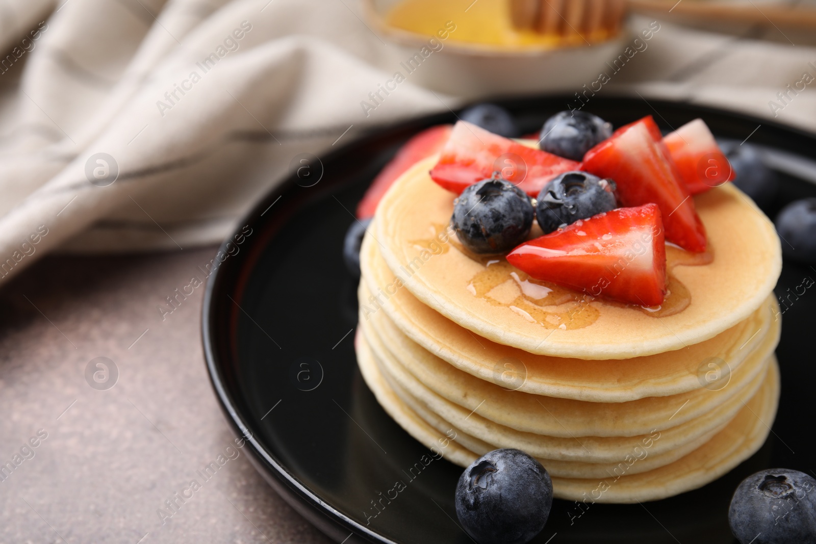 Photo of Delicious pancakes with strawberries and blueberries on brown textured table, closeup. Space for text