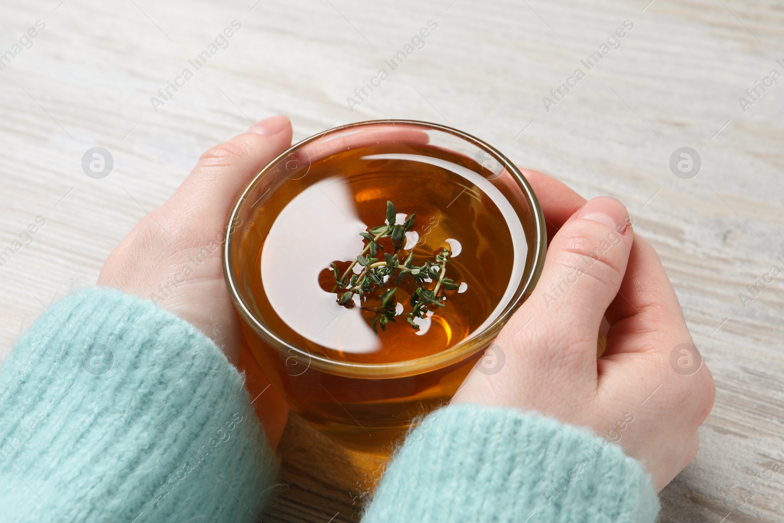 Photo of Woman holding cup of tasty herbal tea with thyme at white wooden table, closeup