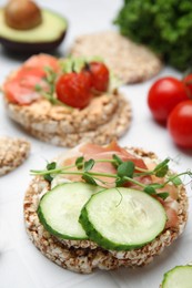 Photo of Crunchy buckwheat cakes with prosciutto, cucumber slices and greens on white table, closeup