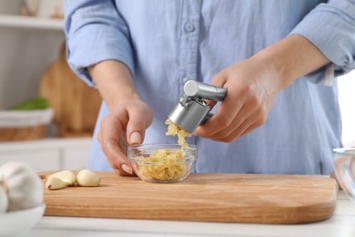 Photo of Woman squeezing garlic with press at white table in kitchen, closeup