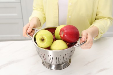 Photo of Woman holding colander with fresh apples at white marble table in kitchen, closeup