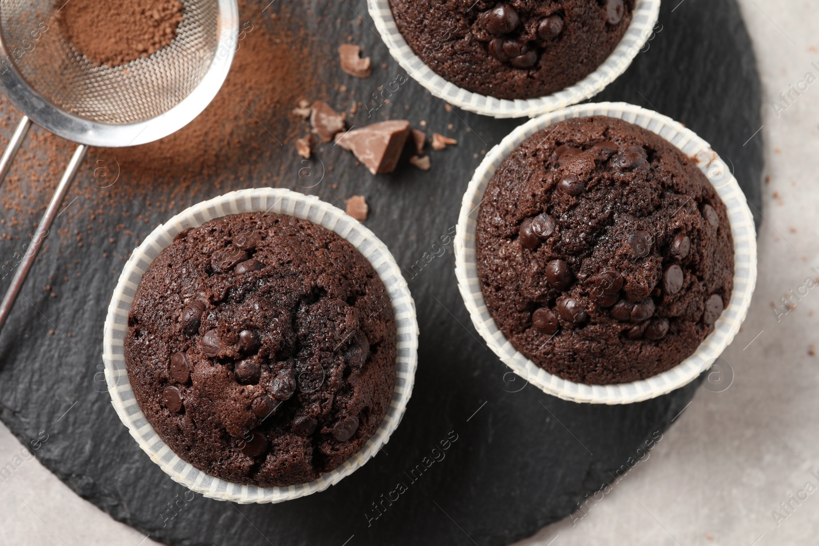 Photo of Delicious chocolate muffins and sieve with cocoa powder on light table, top view