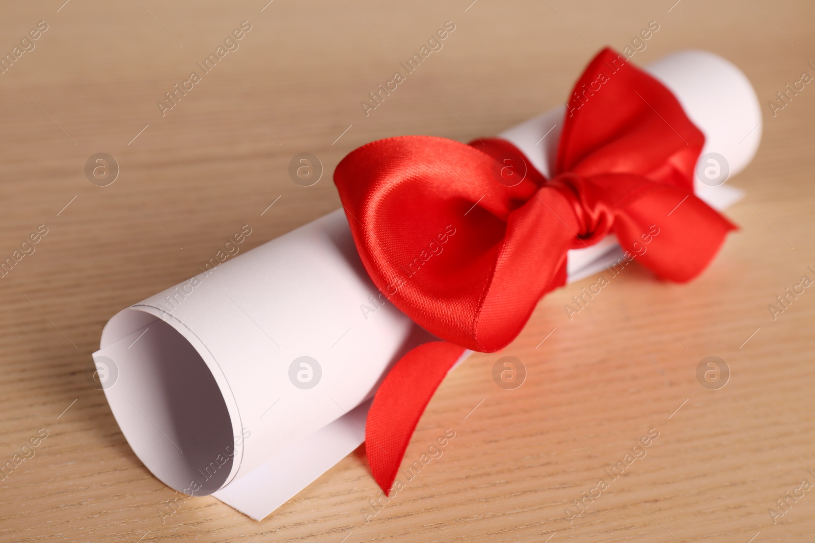 Photo of Graduation diploma tied with red ribbon on wooden table, closeup