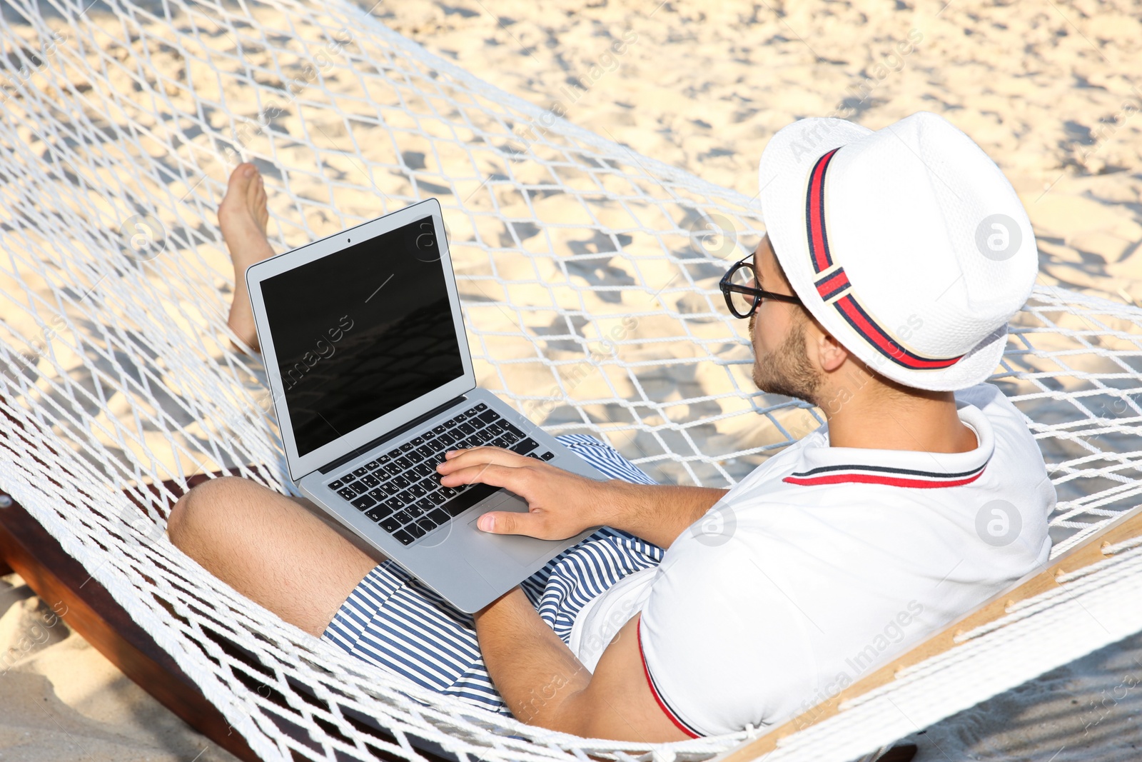 Photo of Young man with laptop resting in hammock at seaside