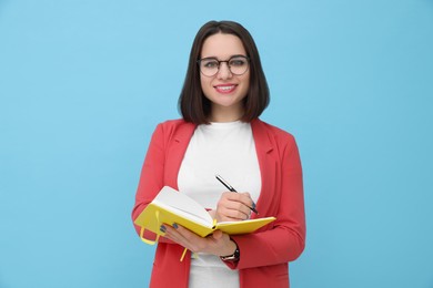 Photo of Happy young intern with notebooks and pen on light blue background