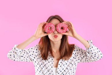 Photo of Beautiful young woman with donuts on light pink background