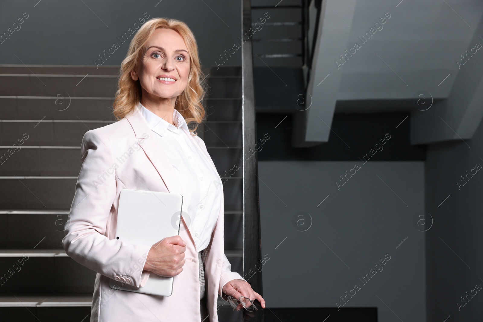 Photo of Happy lady boss with tablet near staircase indoors, space for text. Successful businesswoman