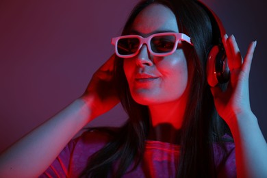 Stylish woman with headphones wearing sunglasses on color background