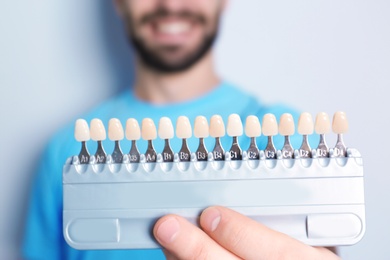 Photo of Young man with teeth color samples against light background, focus on palette