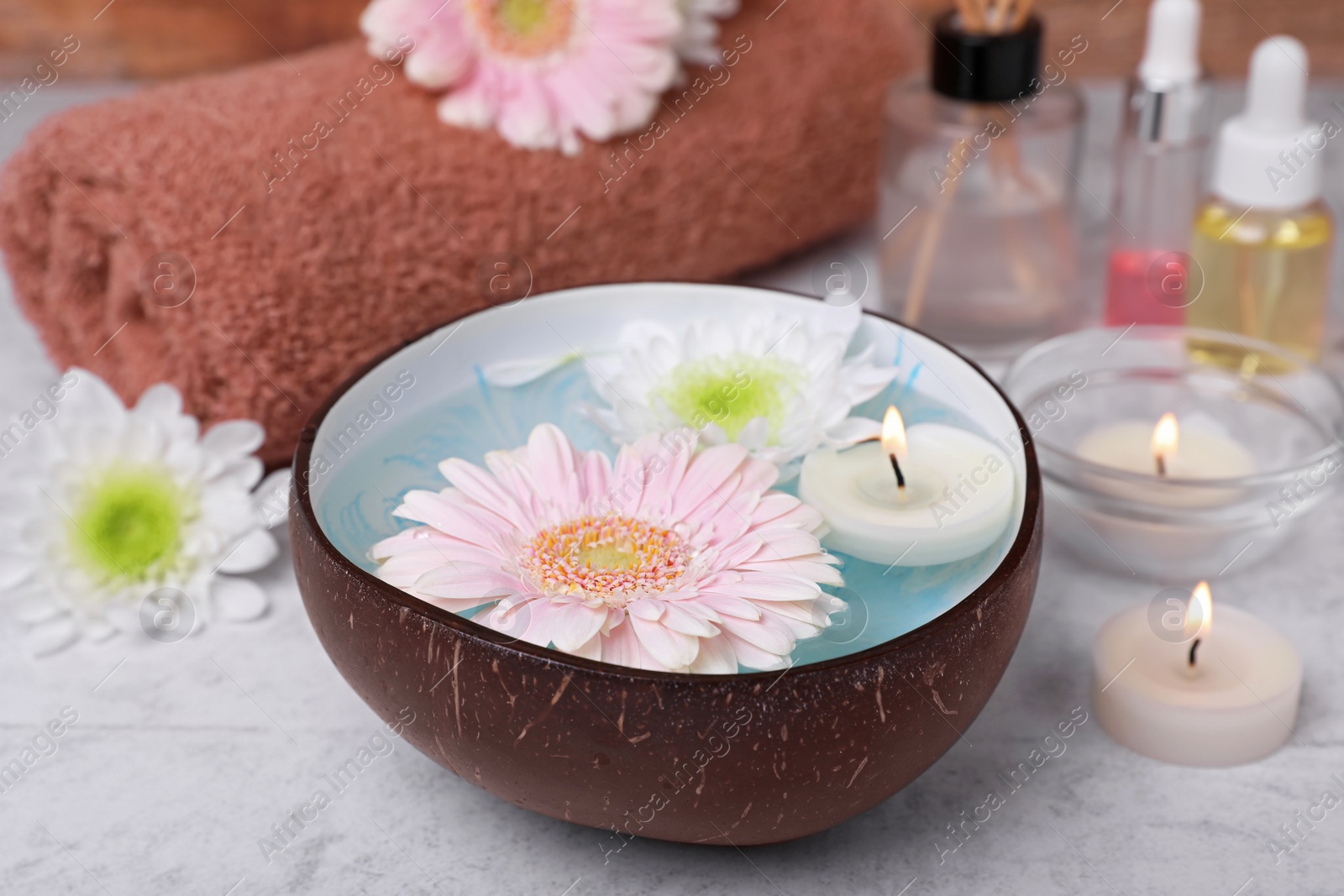 Photo of Beautiful composition with bowl of water, flowers and candles on light table, closeup. Spa treatment