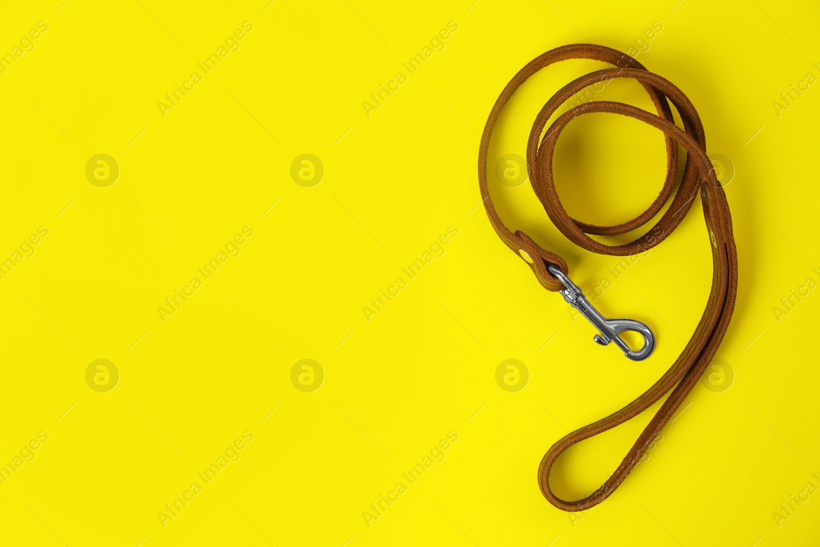 Photo of Brown leather dog leash on yellow background, top view. Space for text