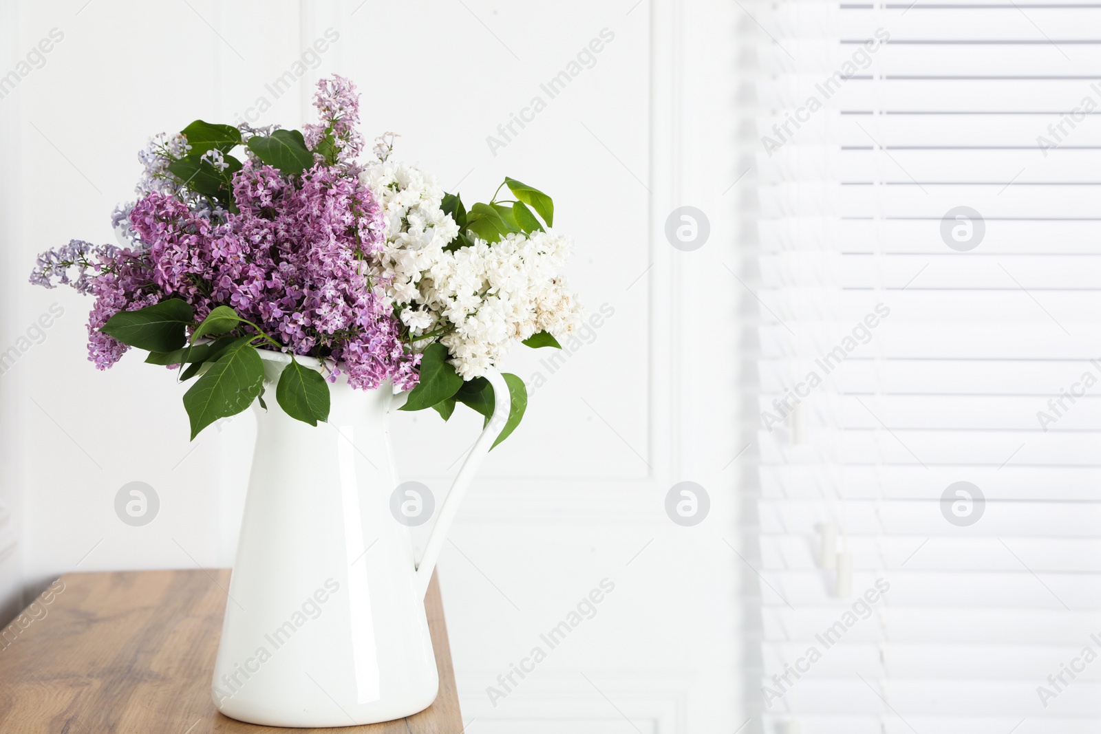 Photo of Beautiful lilac flowers in vase on wooden table near white wall. Space for text