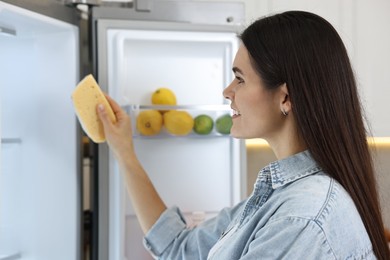 Photo of Young woman taking cheese out of refrigerator in kitchen