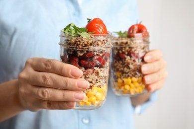 Photo of Woman holding jars with healthy quinoa salad and vegetables, closeup. Space for text