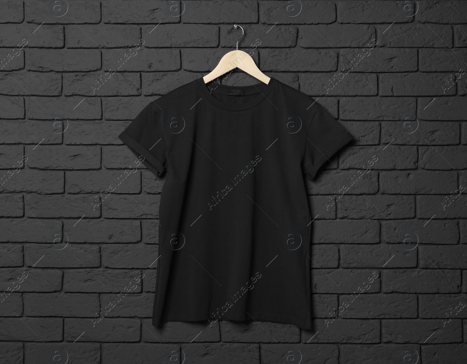 Photo of Hanger with stylish T-shirt on black brick wall