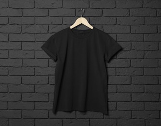 Hanger with stylish T-shirt on black brick wall
