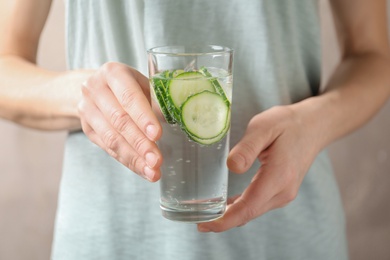 Photo of Young woman holding glass with fresh cucumber water, closeup