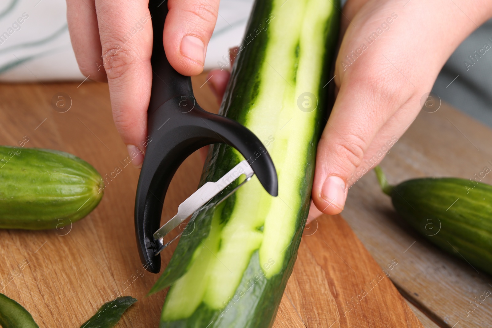 Photo of Woman peeling cucumber at wooden table, closeup