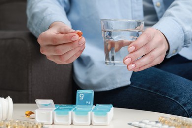 Photo of Woman taking pill from plastic container at white table indoors, closeup