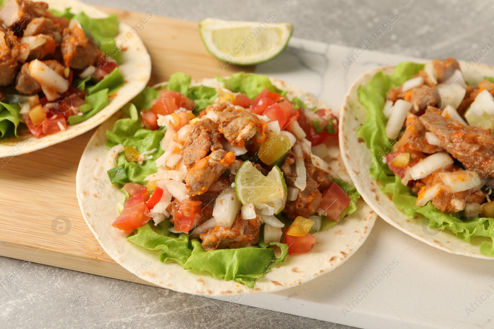 Photo of Delicious tacos with vegetables, meat and lime on grey textured table, closeup