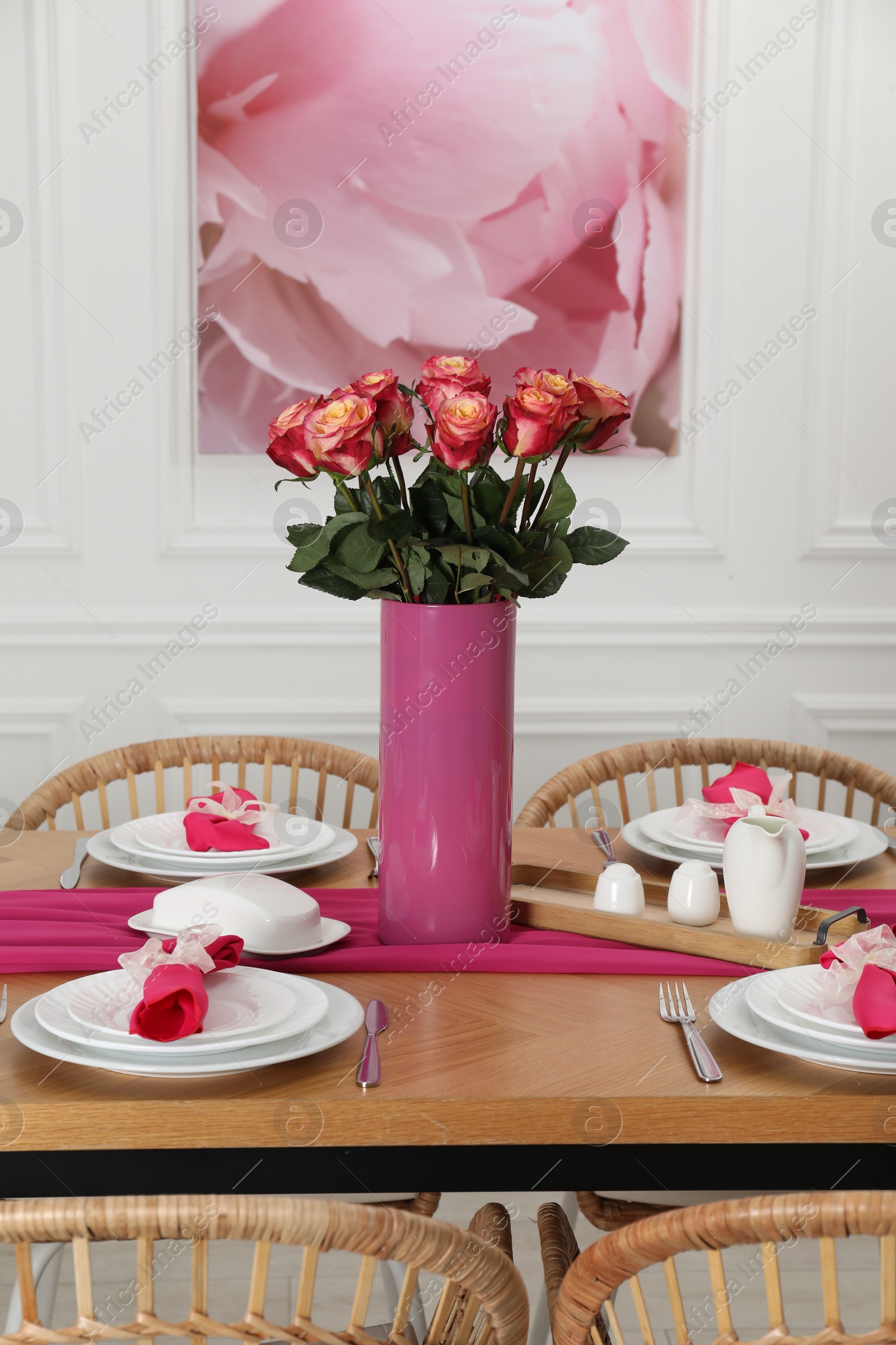 Photo of Color accent table setting. Plates, cutlery, pink napkins and vase with beautiful roses in dining room