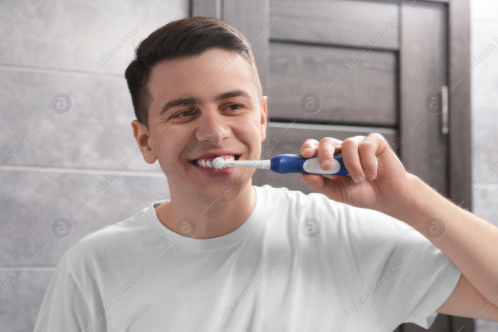 Photo of Man brushing his teeth with electric toothbrush indoors