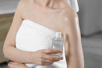 Woman with bottle of body oil on blurred background, closeup