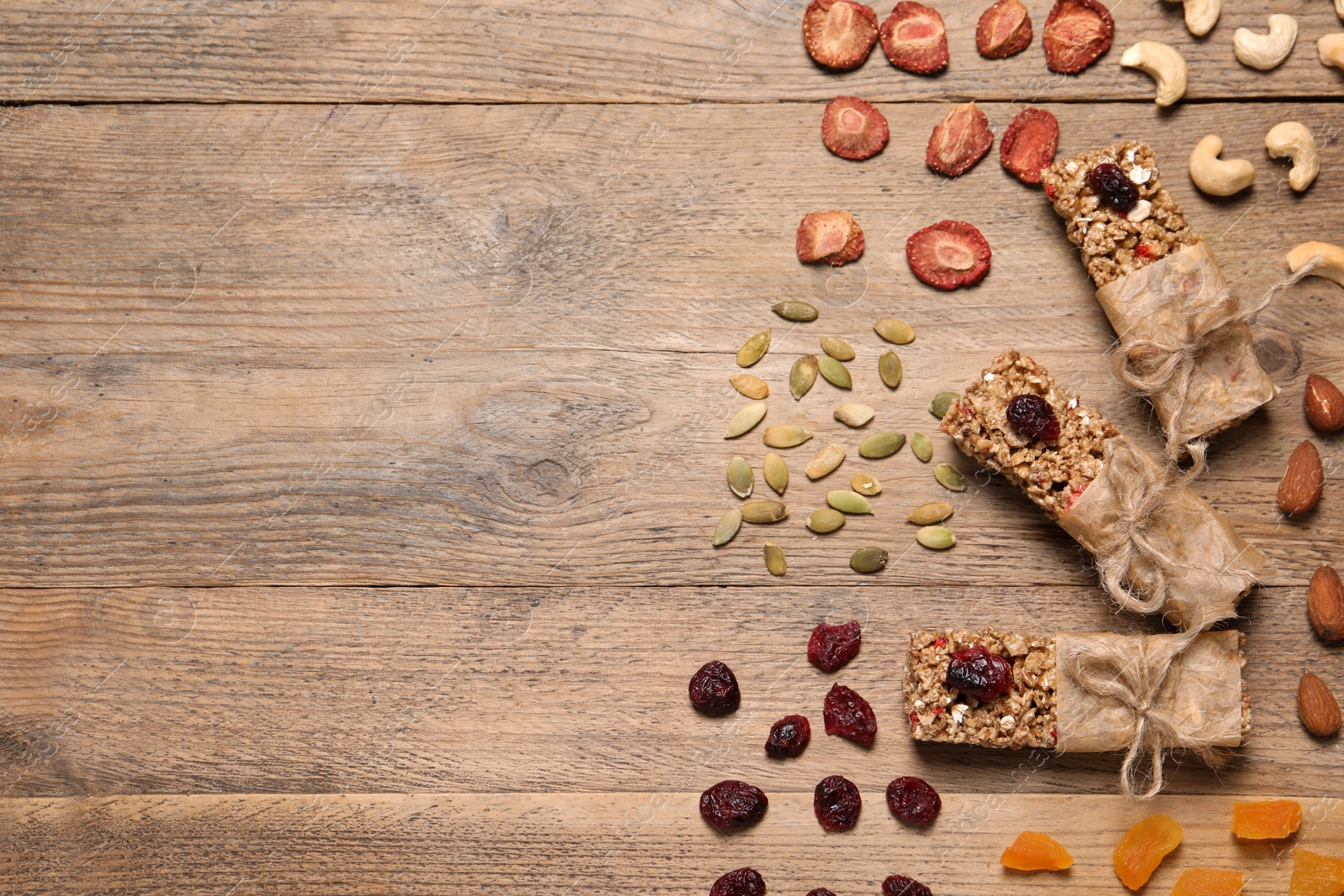 Photo of Tasty granola bars and ingredients on wooden table, flat lay. Space for text