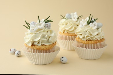 Photo of Tasty Easter cupcakes with vanilla cream and candies on beige background