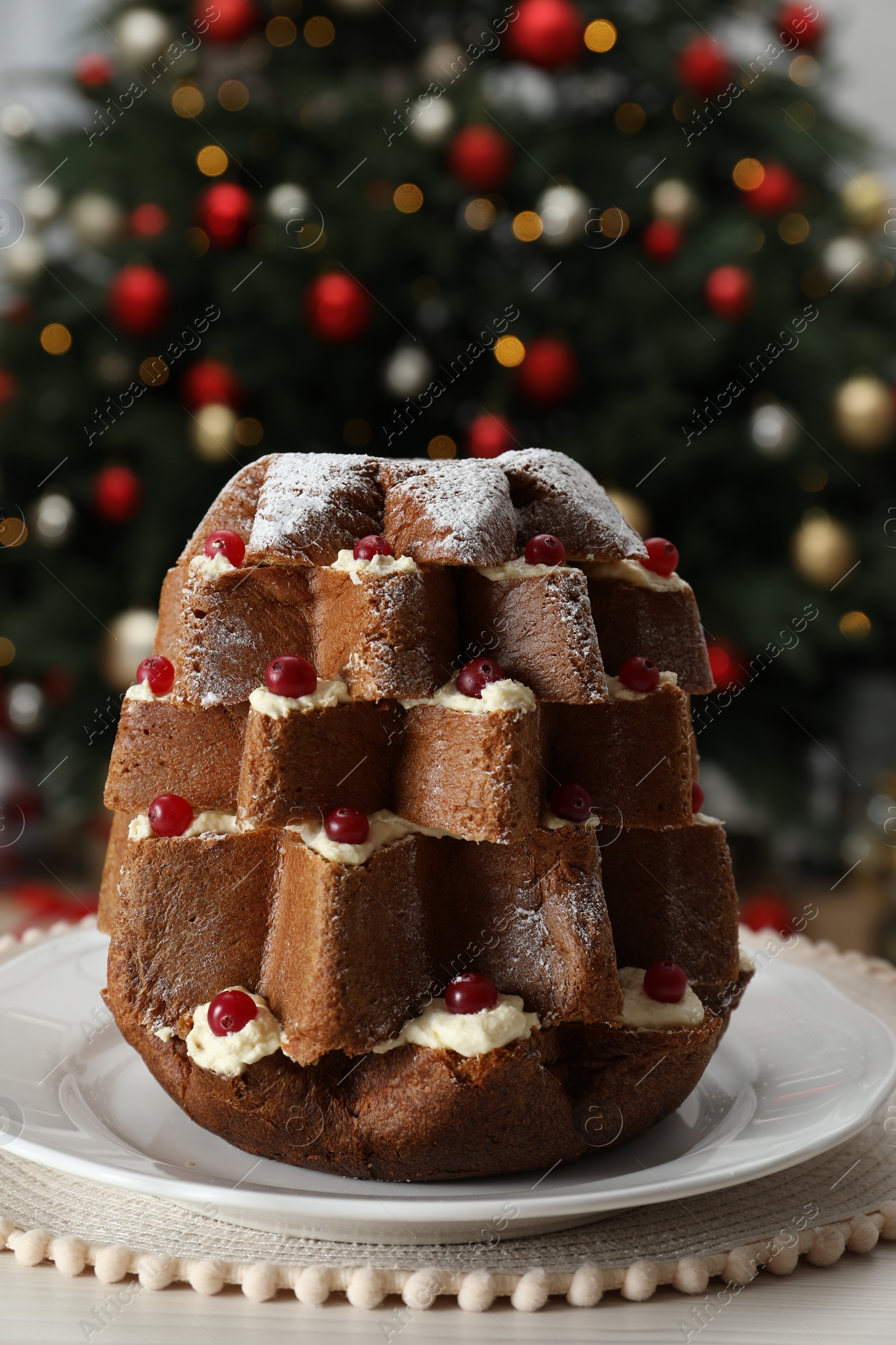 Photo of Delicious Pandoro Christmas tree cake with powdered sugar and berries on white table indoors